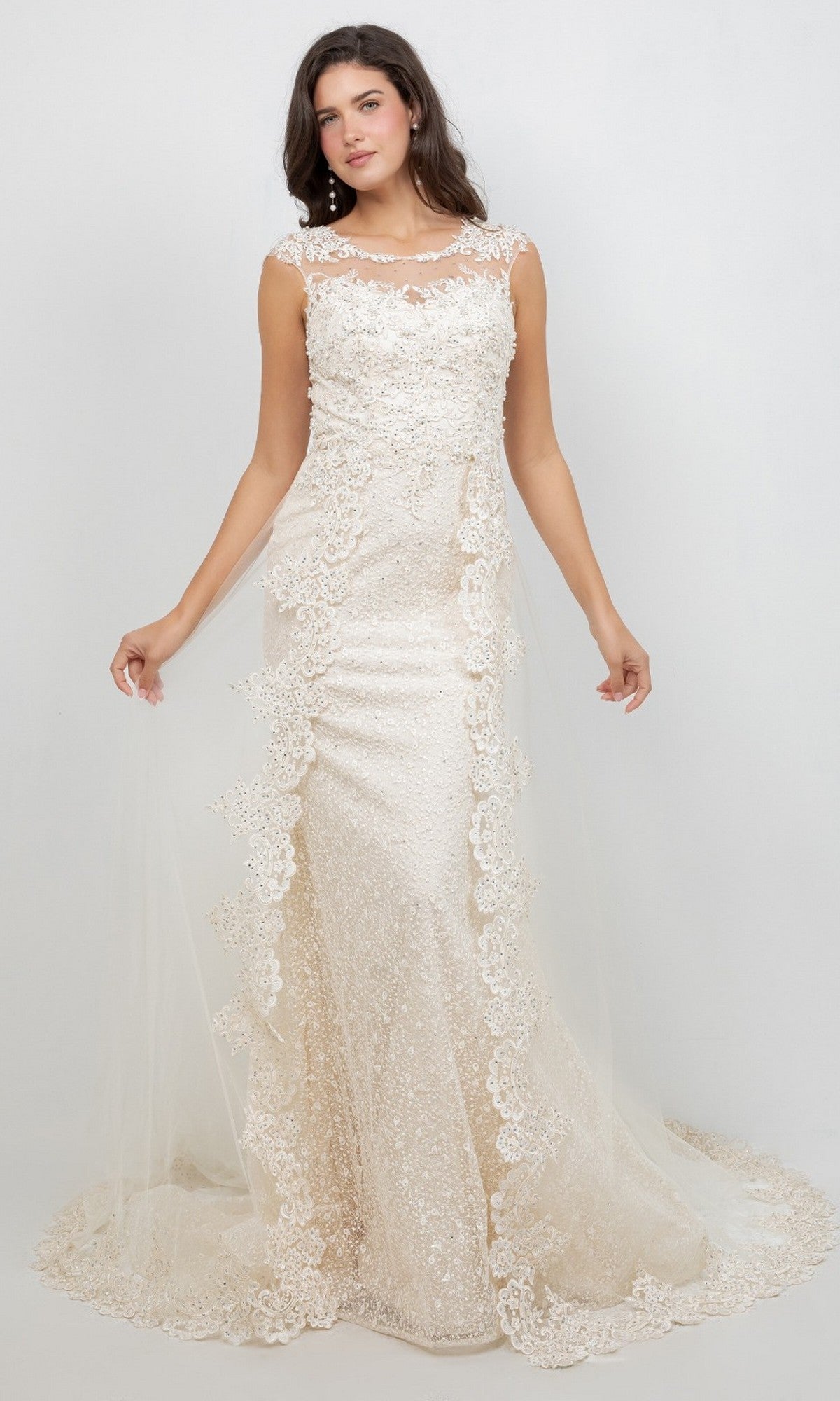 A woman wearing the Cinderella Couture 8506J, a floor-length formal dress featuring sleeveless lace detailing, sequin accents, a sheer tulle overlay, and delicate lace appliques, stands against a plain light background.